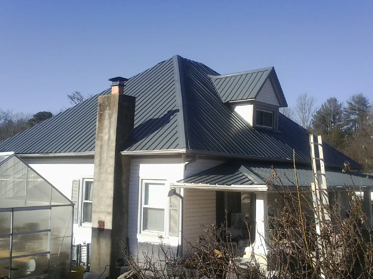 Dark blue standing seam metal roof on a white farmhouse with dormer — Slate & Tile Roof Repair by Roofing Brothers in Tilden