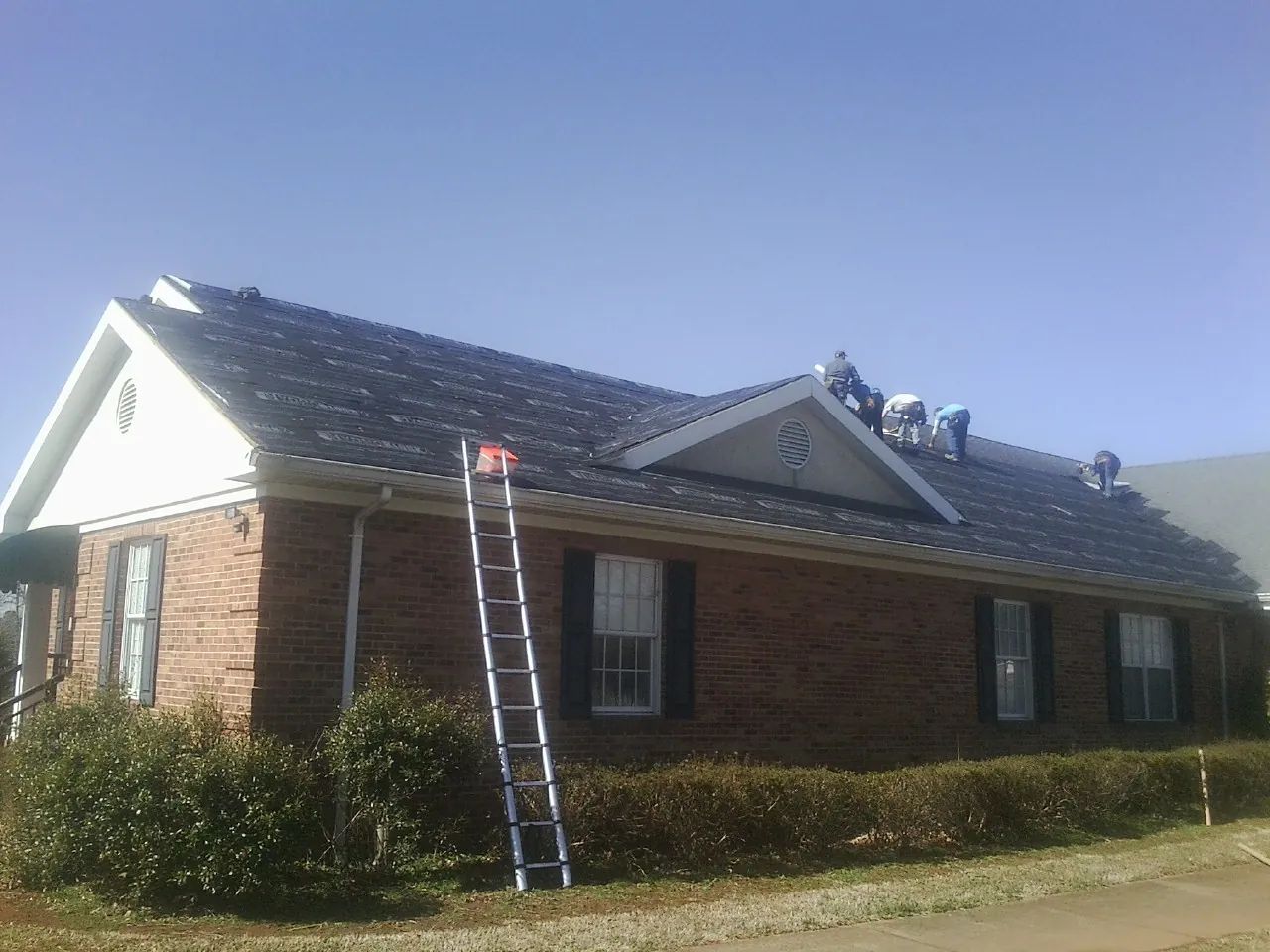 Crew tearing shingles off a brick ranch roof with a ladder set — Emergency Roof Repair work by our crew in Tilden