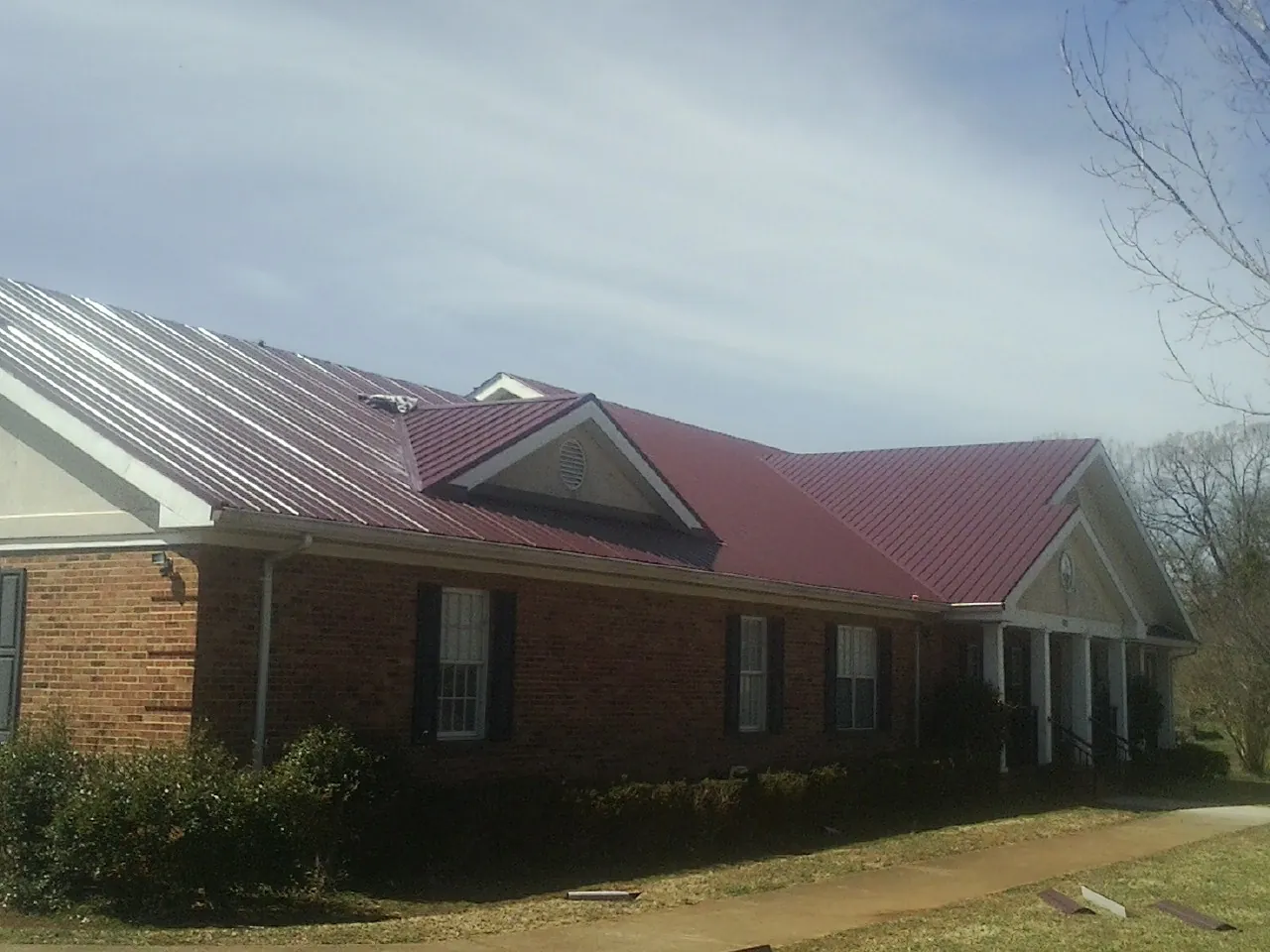 Red metal roof with gabled entries on a long brick building, from a Hail Damage Roof Repair job in Tilden