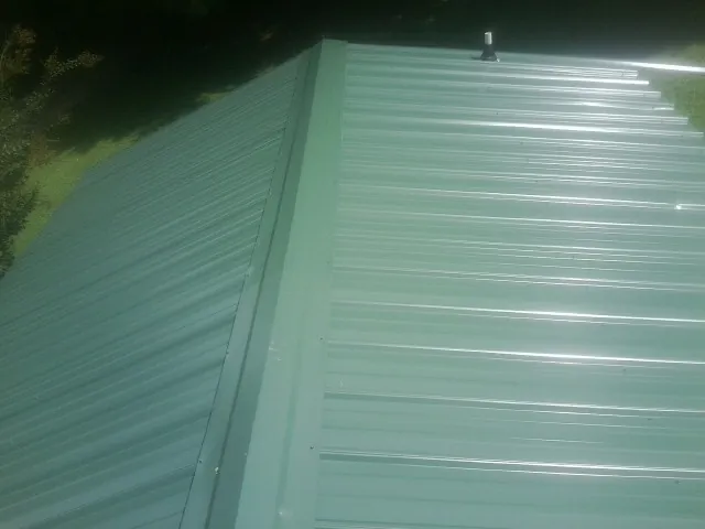 New green metal panels meeting at the ridge of a roof — Flat Roof Repair work by our crew in Tilden