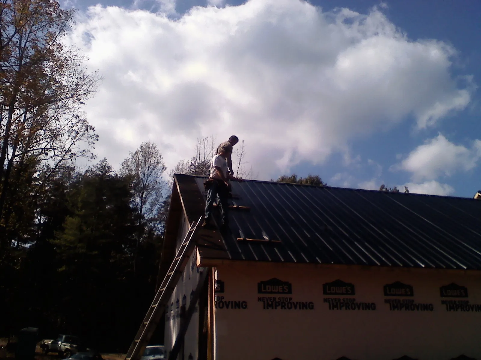 Roofer fastening dark metal panels high against a cloudy sky, from a Roof Inspection job in Tilden