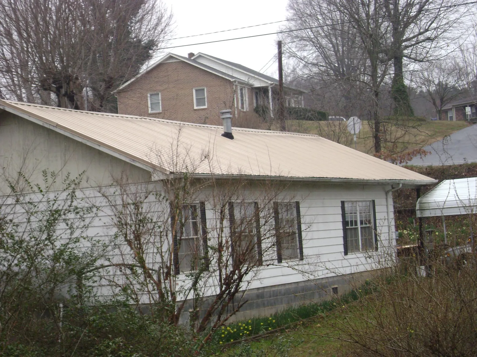 Tan metal roof on a white sided house set into a hillside — Commercial Roofing by Roofing Brothers in Tilden